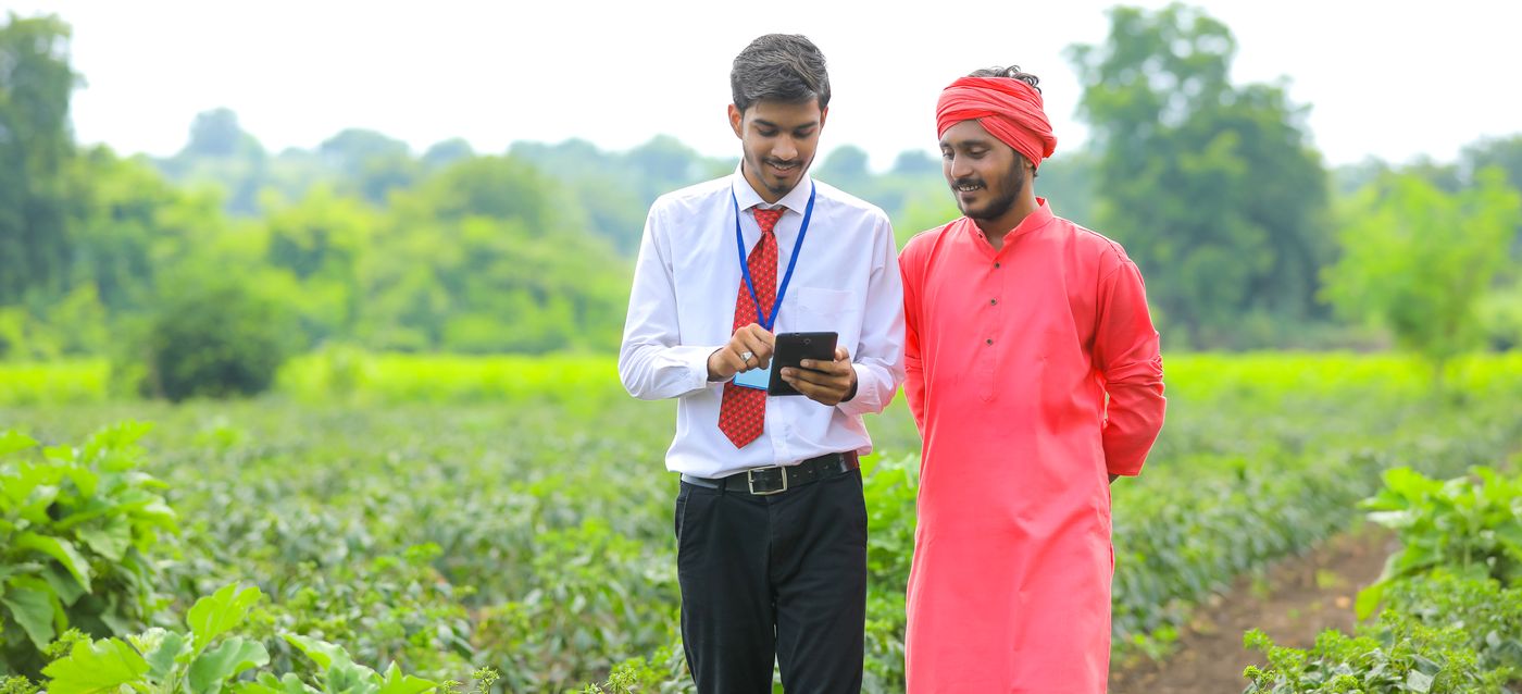 A Vimovi field officer and a grower standing together in a crop, checking intake details on a tablet